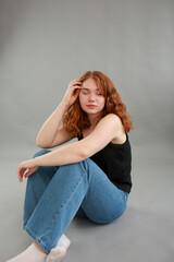 beautiful young girl model redhead. model in jeans and black top on a gray background. studio shooting. model with red hair and unusual appearance.