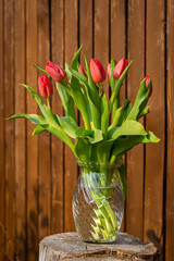 bouquet of red tulips in glass vase on wooden background