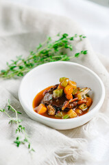 A piece of meat with stewed vegetables cut into cubes. Zucchini, pumpkin and potatoes. Snack in a small white bowl. Сopy space.
