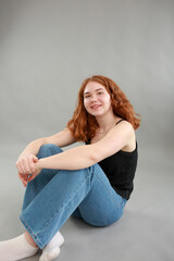 beautiful young girl model redhead. model in jeans and black top on a gray background. studio shooting. model with red hair and unusual appearance.