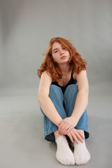 beautiful young girl model redhead. model in jeans and black top on a gray background. studio shooting. model with red hair and unusual appearance.
