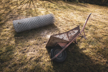 wheelbarrow lies next to a roll of wire mesh fence