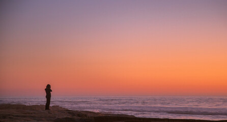 Fototapeta na wymiar solitary woman in twilight at the seashore contemplates the ocean