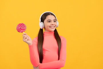 happy child listen music in headphones with lollypop on yellow background, music