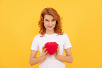 smiling redhead woman hold love heart on yellow background, 14 february