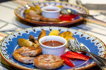 Fried sausages with potatoes and tomato sauce are on a plate