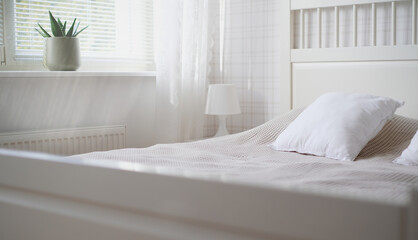 The interior of the room in white tones with a bed, bedside table, table lamp and a flower on the windowsill