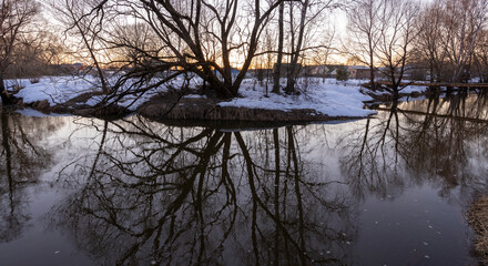 Sunset through the trees, reflection in the water. Spring rural. Mystical evening landscape by the river.