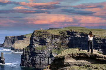 A women admires the Cliffs of Moher views, sea cliffs located at the southwestern edge of the Burren region in County Clare, Ireland - obrazy, fototapety, plakaty