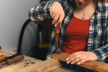Close-up cropped shot of the hands of a young red-haired carpenter using a screwdriver on a wooden board.