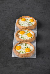 Small open rye cottage cheese pies with mozzarella, quail eggs and dill, on paper. Dark gray background