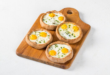 Mini open rye cottage cheese pies with mozzarella, quail eggs and dill, on a wooden board. White background.