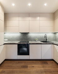 Vertical photo of Kitchen interior with designer white cabinets with black faucet and black oven and hob. Kitchen design inside the apartment.