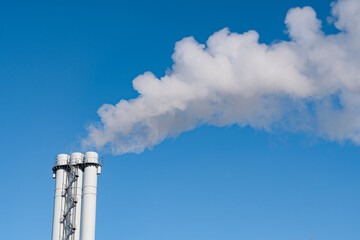 Air pollution by smoke coming out of pipes against blue sky. Concept of pollution, environmental problems and emissions