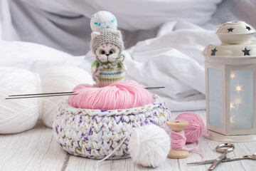 a knitted kitten with knitting needles, colored balls of thread in a basket. Creative workshop on needlework handmade