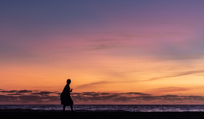 woman walking along the shore of the beach at sunset