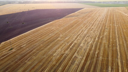 Aerial drone view flight over field after harvest with cars haystacks and dug up plowed field. Yellow brown farmland lands. Top view. Rural landscape and scenery country. Countryside plantations