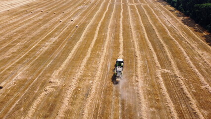 Obraz premium Hay bale tractor. Tractor harvesting hay into bales in field on sunny day. Aerial drone view. Tractor drives across field and makes bales from cut straw. Field and agricultural work, baler. Ukraine