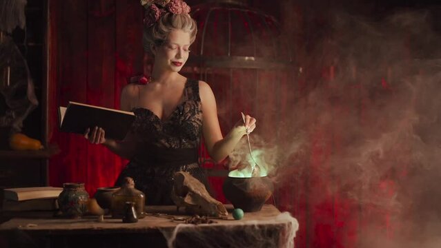 Halloween witch with cauldron and magic book. Beautiful woman flowers in hair conjuring, making witchcraft. Standing spooky dark room. Enchantress prepare love potion Slow motion. Handheld