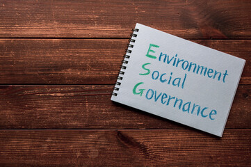 There is sketchbook with the word Environment, Social, Governance. It's placed on a wood board.