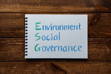 There is sketchbook with the word Environment, Social, Governance. It's placed on a wood board.