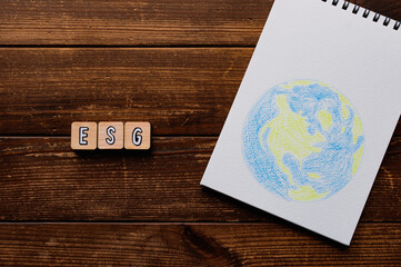 There is word cube formed the word ESG. It's placed on a wood board with an illustration of the earth.