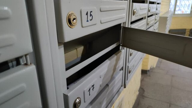 The man opens the mailbox with a key. Gray mailboxes close-up in a modern apartment building, residential real estate. Checking mail. Mailboxes for letters, newspapers and magazines