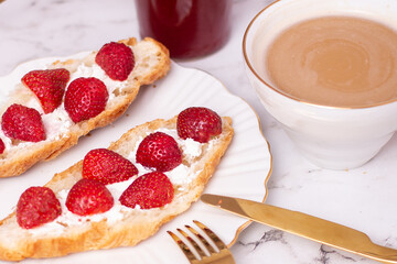 Coffee cup and sweet croissant with fresh strawberry on white table