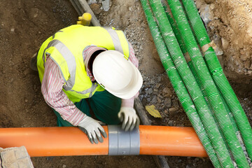 worker installing hdpe corrugated electric and sewer pipes at the construction site on street city - 497984900