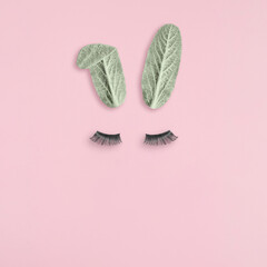 Bunny rabbit face made of natural green leaves with eyelashes on pastel pink background.Happy Easter minimal concept.Flat lay.