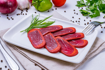 Dried sliced basturma on a white plate on white table