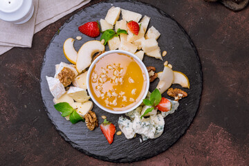 assorted European cheeses on black plate with honey top view