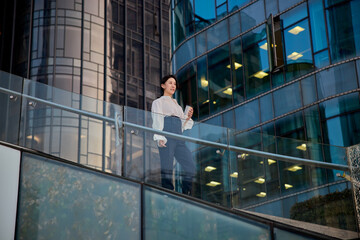 Portrait of confidence Asian businesswoman looking away and having coffee in front of modern office buildings.