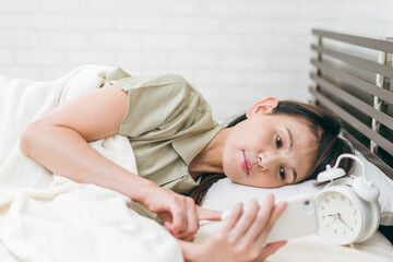 ベッドルームでスマホを見るミドル世代の女性
