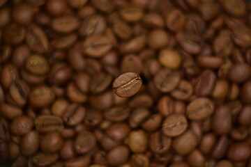 Top view on natural roasted coffee bean close up hovering in frozen motion on blurry background of coffee beans. Selective soft focus, twisted bokeh effect