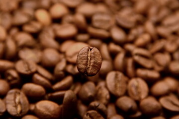 Side view on natural roasted coffee bean close up hovering in frozen motion on blurry background of coffee color of heap beans. Selective focus, bokeh effect