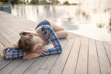 Woman wear one piece swimsuit laying near pool at beach, sunset moment.
