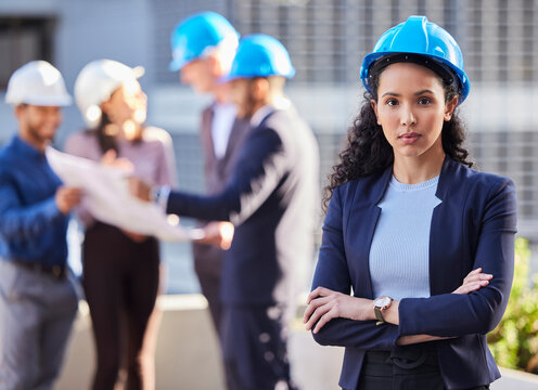 My team can handle anything. Shot of a young businesswoman standing with her arms folded and wearing a hardhat while her colleagues stand behind her.