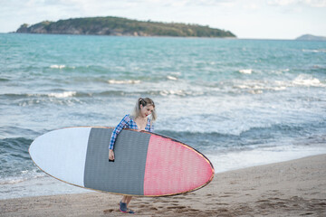 Woman wearing one-piece swimsuit hold sup board or paddle board to the sea.