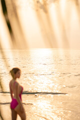 Blur woman wearing pink one piece swimsuit enjoy romantic sunset moment under the coconut trees on tropical beach.
