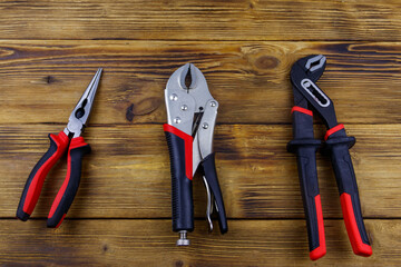 Set of different pliers on wooden background. Top view