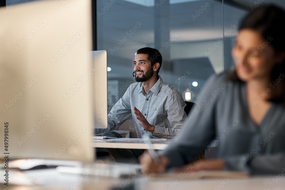 Poster Creating happy customers is a 247 commitment. Shot of a young man using a headset and computer late at night in a modern office.