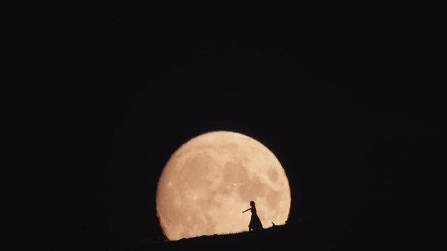Silhouette of dancing woman against huge moon background at night. 