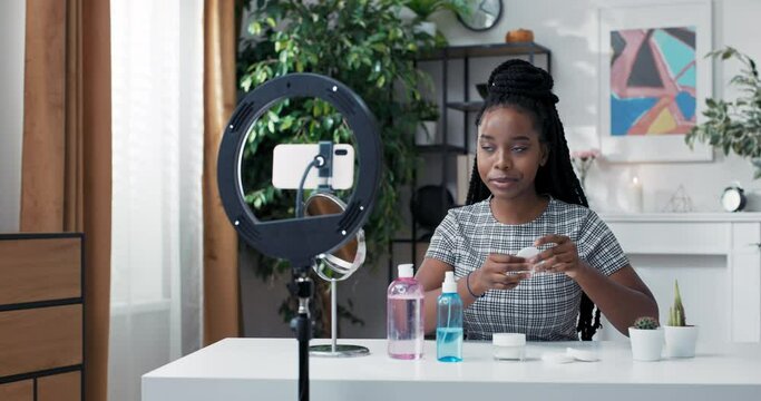 Female influencer records a vlog on social media of her skincare routine. A girl with dark skin takes a cotton ball and makeup remover. Tutorial on how to properly cleanse skin of cosmetics.