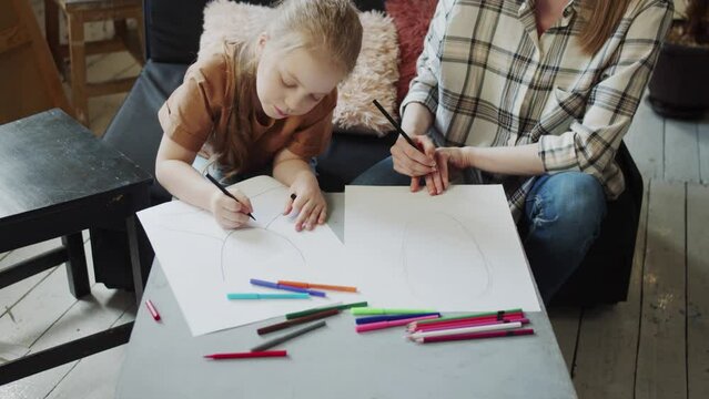 The nanny invited the child to draw a portrait of his mother. Girl draws with pencils on a piece of paper