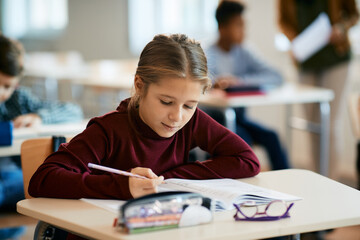 Schoolgirl writing in notebook during class in the classroom.