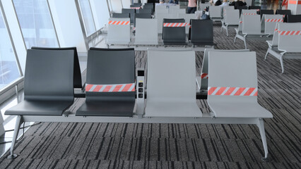 Fototapeta na wymiar Empty chair in airport terminal, departure with red and white distance ribbons due coronavirus post covid-19 virus outbreak. Departure New social travel distancing normal. Pandemic and tourism concept
