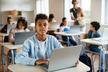Black elementary student learns on laptop during computer class and looking at camera.