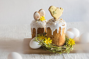 Traditional easter cake decorated with easter cookies, willow twigs in shape of nest, yellow flowers, white eggs on linen tablecloth. Side view, selective focus. Easter treat, holiday symbol