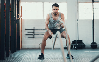 Plakat Im feeling the burn. Shot of a young man using the ropes in the gym to build arm strength.